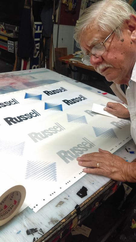 Sign maker hand-finishing cut vinyl lettering at the shop bench