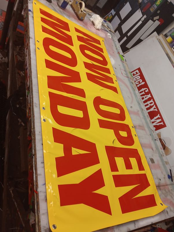 Bright yellow Now Open vinyl banner for a grand opening